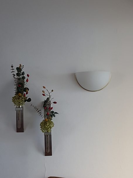 Zwei Blumenvasen an der Wand mit bunten Blumen und eine runde Wandlampe darüber.