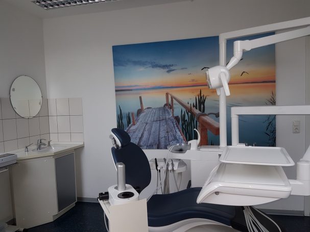 Zahnarztpraxis mit modernem Behandlungsstuhl und Landschaftsbild an der Wand.
